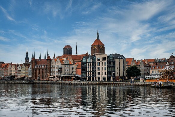 Historische Häuserfassaden am Flussufer in der Altstadt von Danzig bei blauem Himmel.